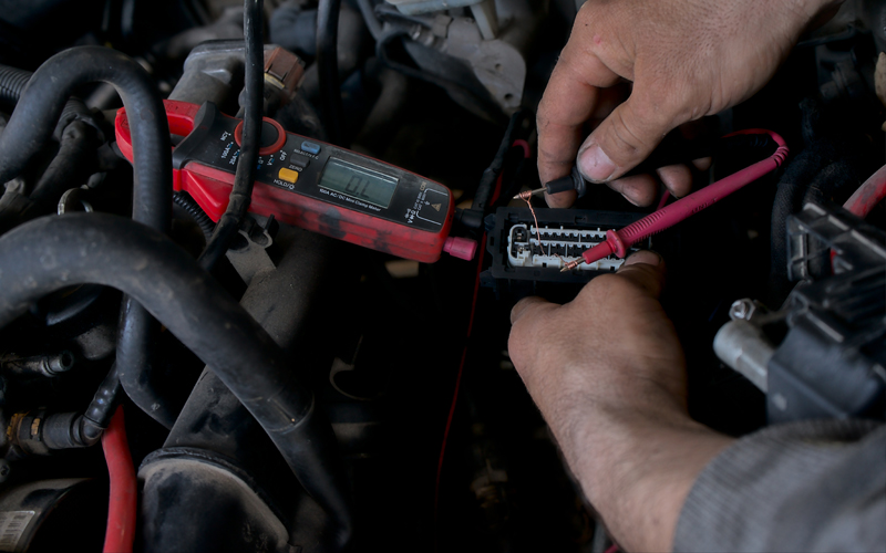 An Auto Electrician Using A Measuring Device To Check The Voltag An Auto Electrician Using A Measuring Device To Check The Voltag